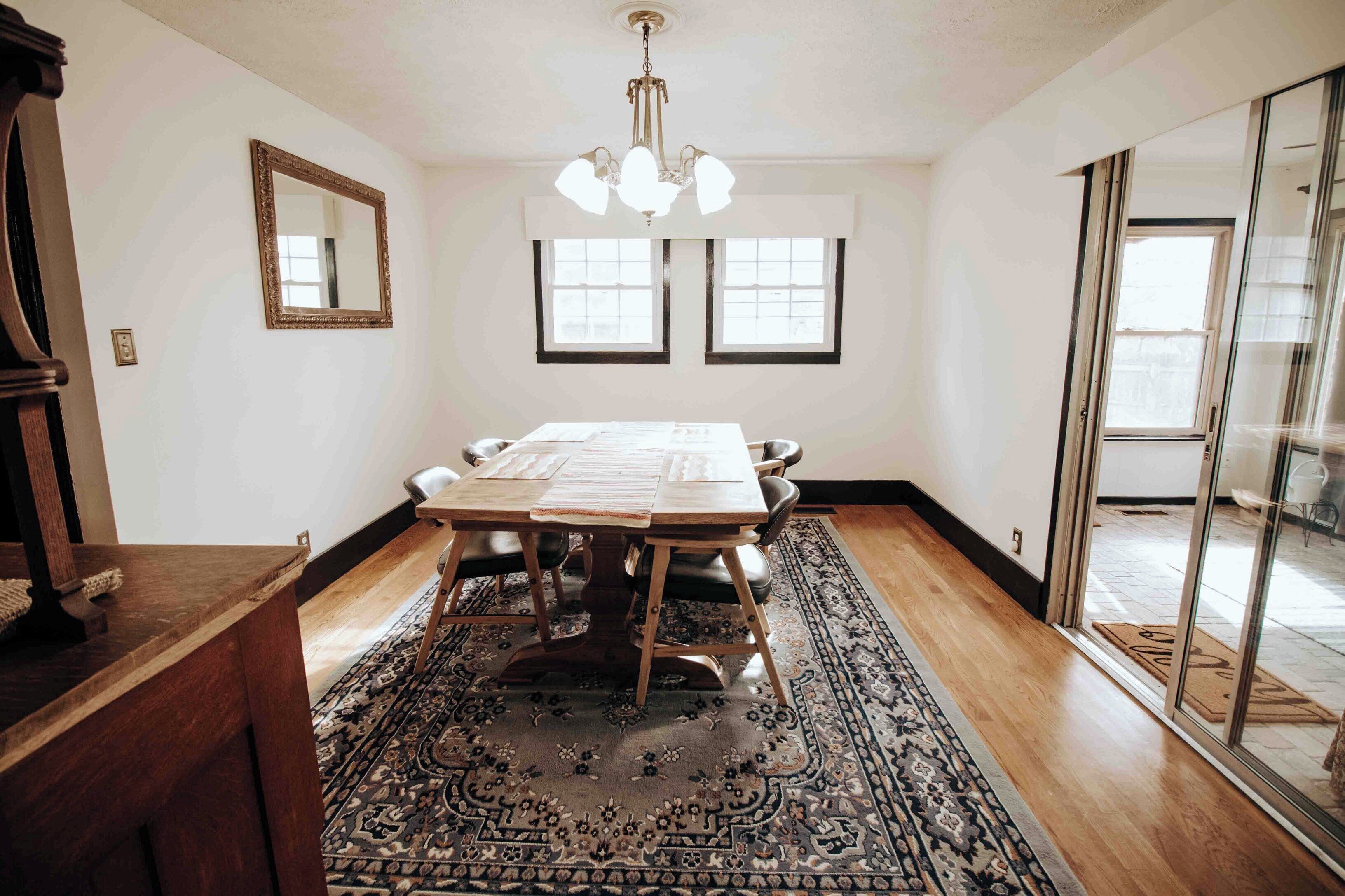 A dining area with a wooden table, chairs, a chandelier, and a patterned rug.