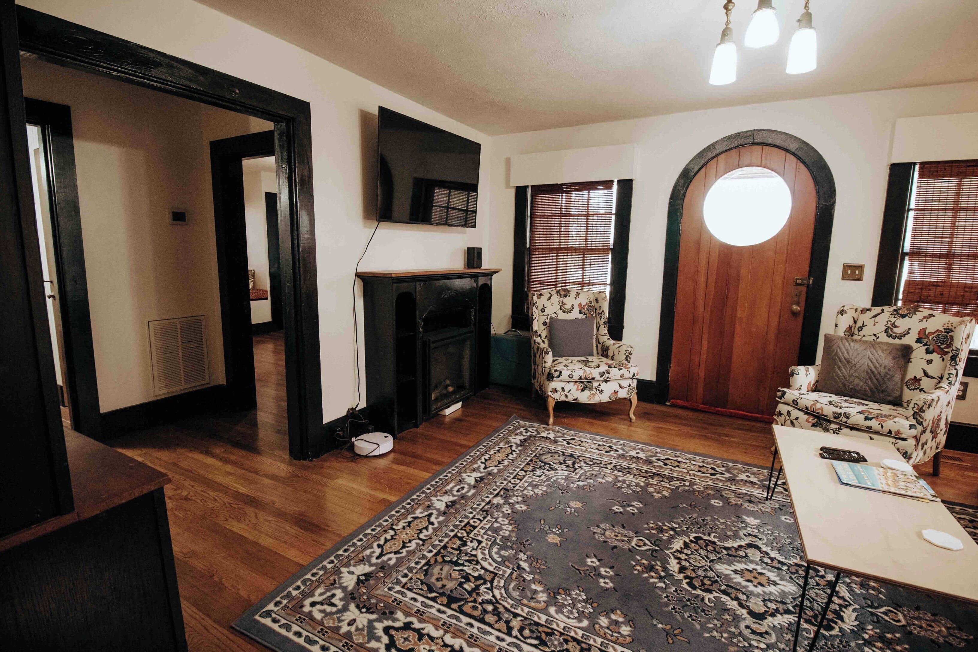 A living room with a fireplace, two armchairs, a coffee table, and a TV mounted on the wall.