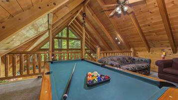 A pool table in a wooden room with a sloped ceiling and a ceiling fan.
