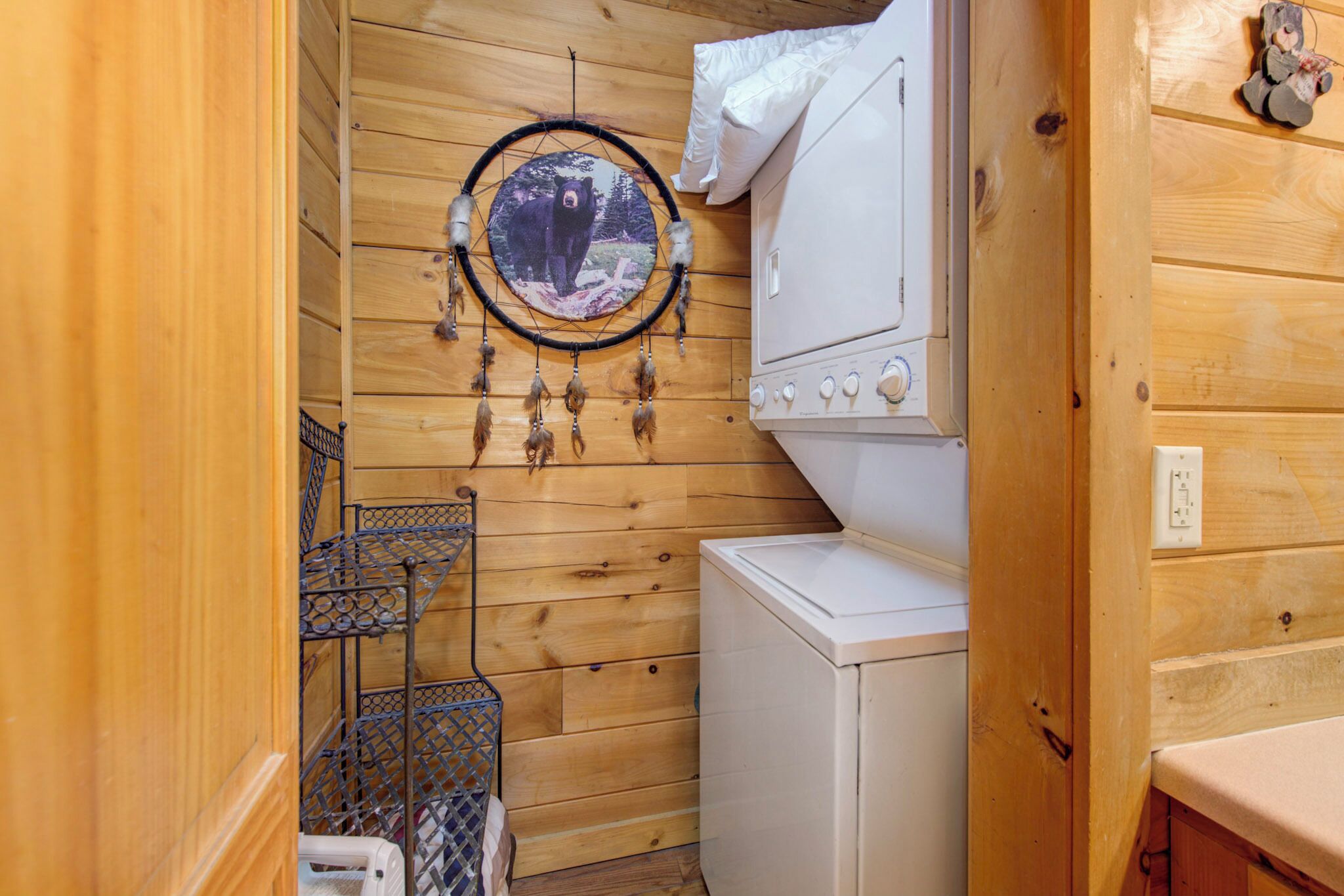 A compact room with wooden walls, a washing machine, a drying rack, and a dreamcatcher.