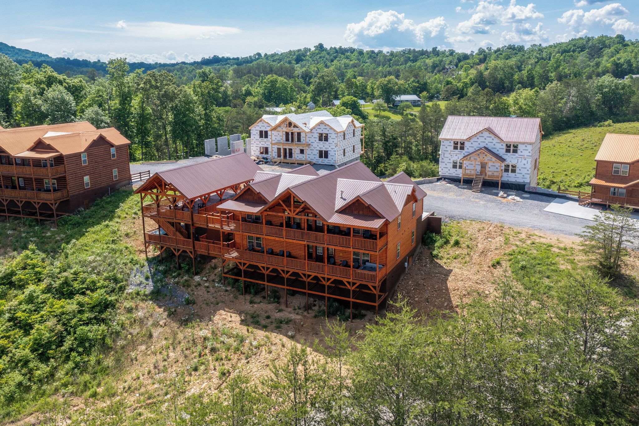 A large wooden building with multiple balconies and a covered outdoor area, surrounded by lush greenery and hills.