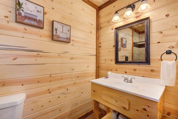 A wooden cabin bathroom with a white sink, a mirror, and framed pictures on the wall.