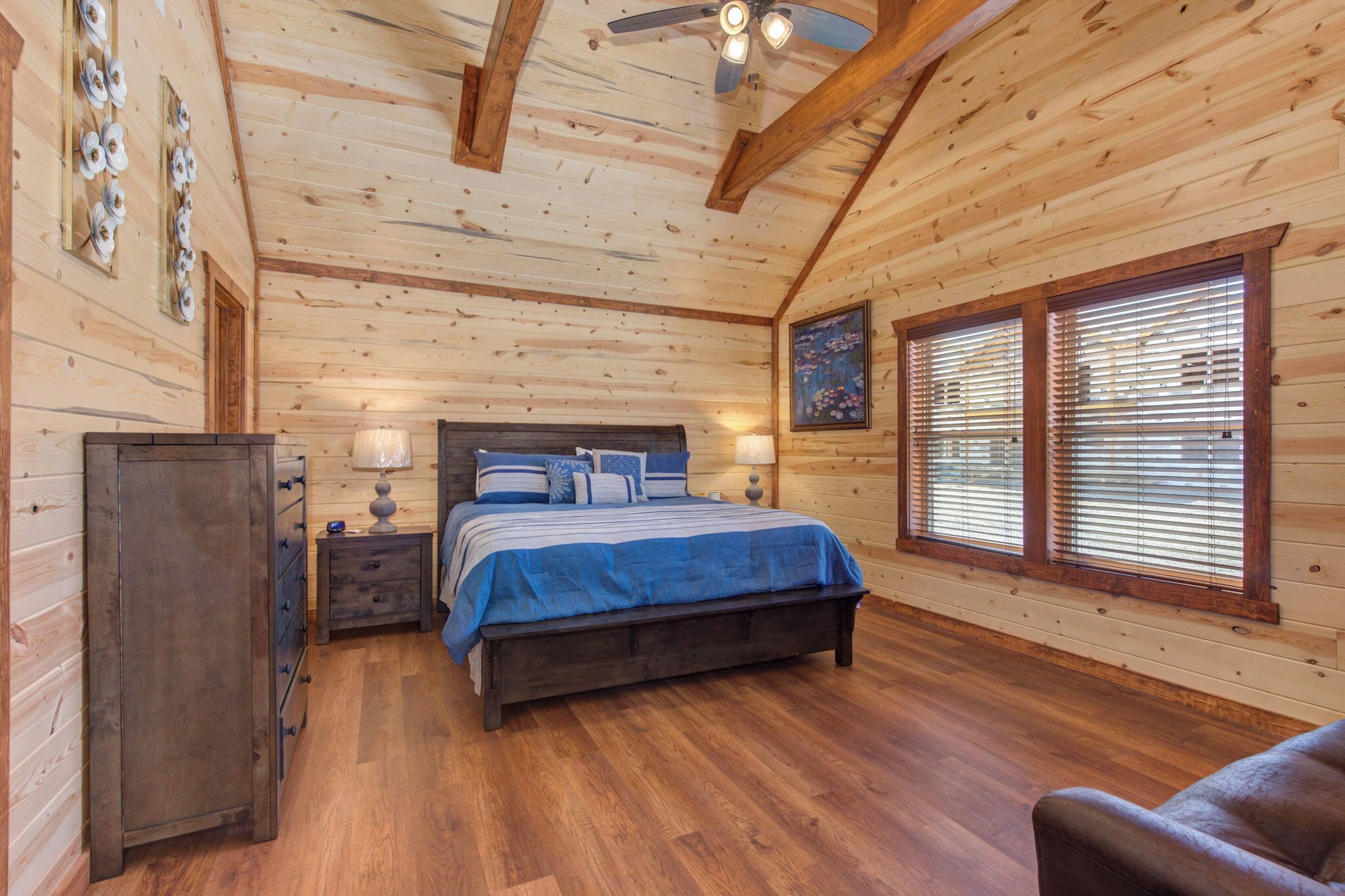 Ein Schlafzimmer einer Holzhütte mit Bett, Nachttischen, einem Kleiderschrank und einem Fenster mit Jalousien.