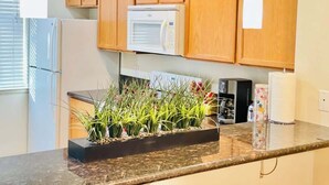 Une cuisine avec des meubles en bois, un four à micro-ondes, un réfrigérateur, une machine à café et une plante sur le plan de travail.