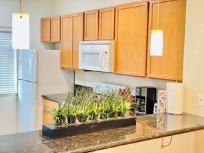 A kitchen with wooden cabinets, a microwave, a refrigerator, a coffee maker, and a plant on the counter.