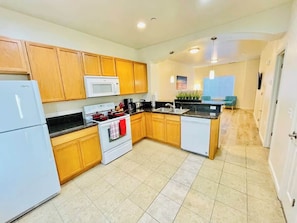 A compact kitchen with wooden cabinets, a white refrigerator, a microwave, and a stove. - 2 Bd, 2.5 Baths, Sleeps 6/G9 (Reno)