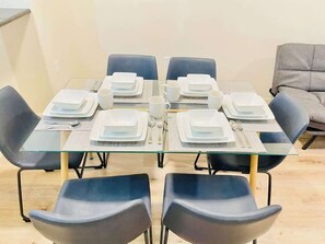 Mesa de comedor dispuesta para seis personas, con sillas negras, cubierta de vidrio y platos blancos.