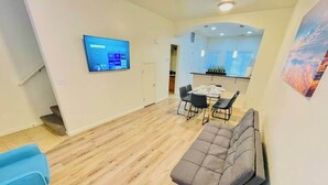 Un salon moderne comprenant un canapé, des fauteuils, un téléviseur et un coin repas avec une table et des chaises.