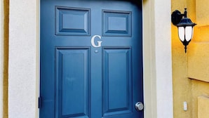 Une porte bleue ornée d’une lettre « G » et un luminaire fixé au mur.