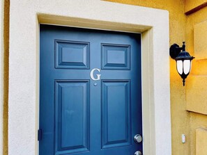 A blue door with a letter 'G' and a wall-mounted light fixture.
