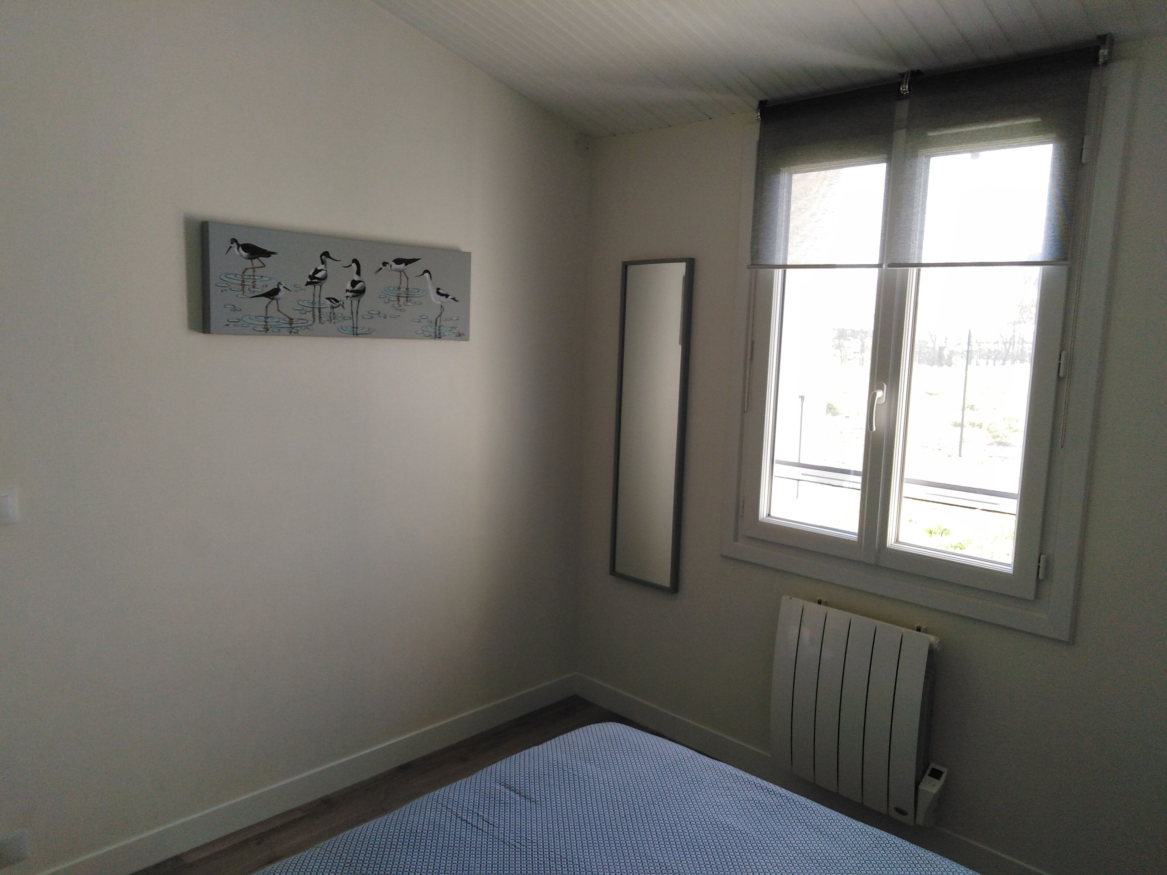 Une chambre à coucher comprenant un lit, une fenêtre, un radiateur et une œuvre d’art accrochée au mur.