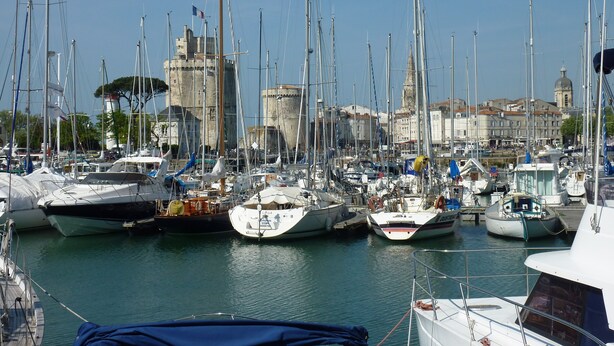 A marina with multiple boats docked, a historic tower, and a church in the background. - Le Figuier, Gite Rural du Seuil, Near La Rochelle (Villedoux)