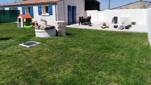 A house with a tiled roof, a small patio with outdoor furniture, and a garden area with flowers and plants. - Le Figuier, Gite Rural du Seuil, Near La Rochelle (Villedoux)