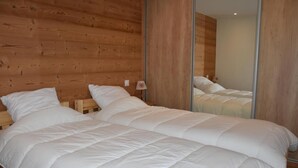 A double bed with white bedding in a room with wooden paneling and a mirror reflecting the bed. - Balcony, fireplace or stove, tv, 88m², Pralognan-la-Vanoise (Pralognan-la-Vanoise)
