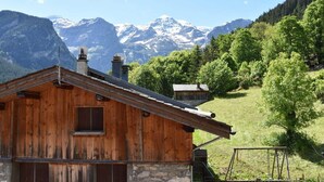 A wooden cabin with a stone foundation, set against a backdrop of snow-capped mountains and lush greenery. - Balcony, fireplace or stove, tv, 88m², Pralognan-la-Vanoise (Pralognan-la-Vanoise)