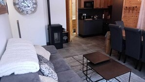 Ein modernes Wohnzimmer mit einem grauen Sofa, einem kleinen Couchtisch und einer Küche im Hintergrund.