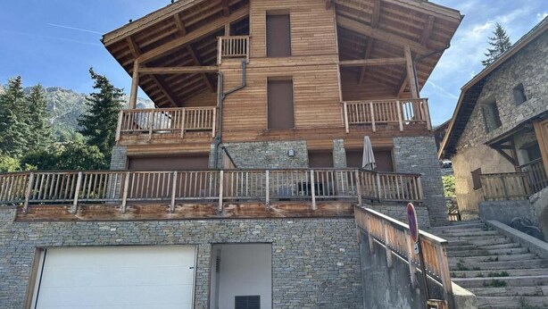 Ein mehrstöckiges Holzgebäude mit Balkonen, einer Garage und Steinmauern.