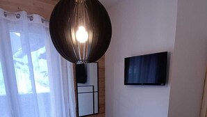 Ein Schlafzimmer mit einem Bett, einer runden Pendelleuchte, einem an der Wand befestigten Fernseher und einem kleinen Holzschemel.