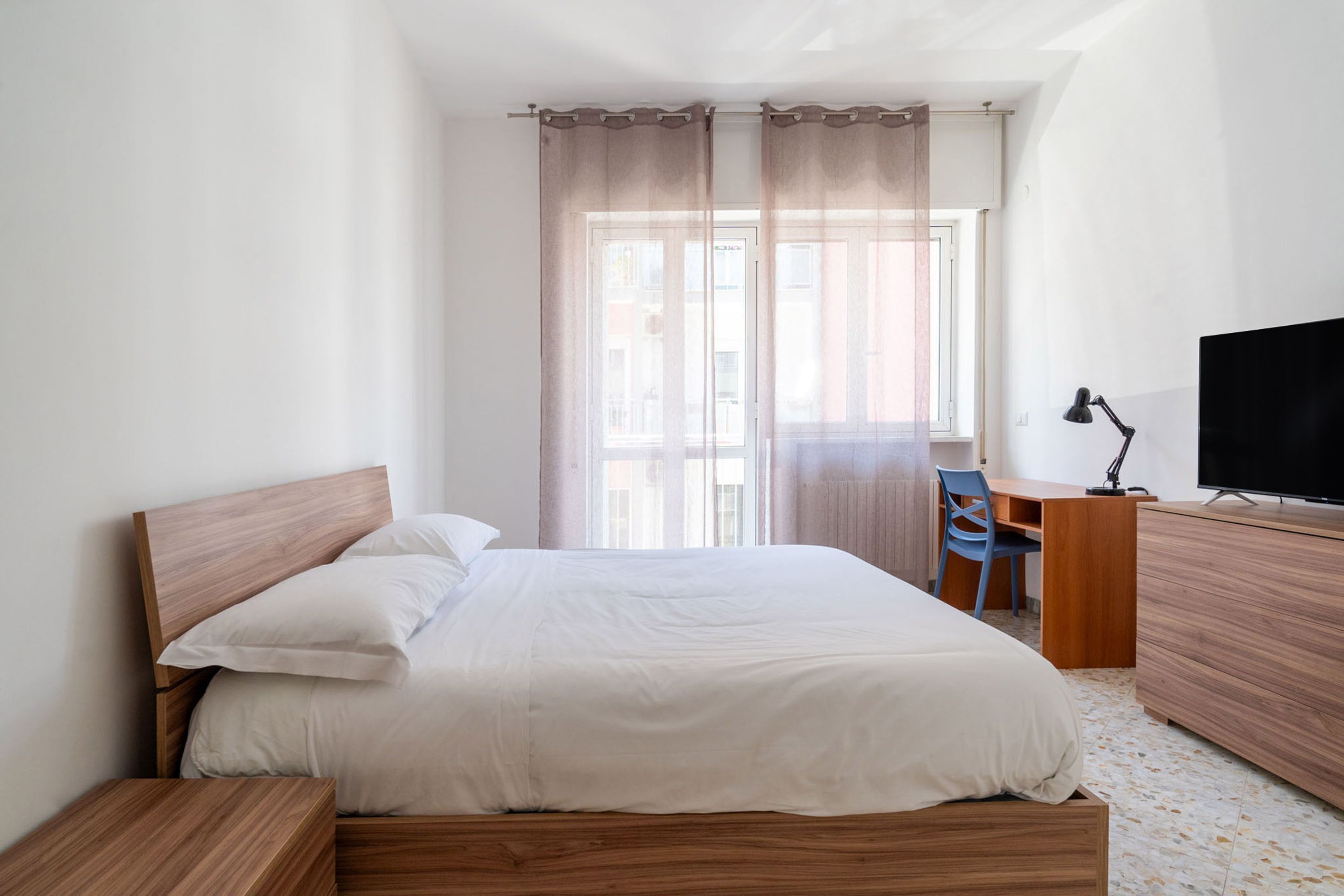 A neatly arranged bedroom with a wooden bed, a desk, and a television.