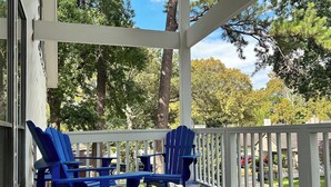 A covered porch with blue Adirondack chairs and a white railing.