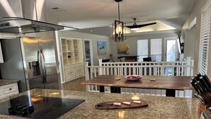 A modern kitchen with granite countertops, a stainless steel refrigerator, and a wooden dining table with a bowl of fruit.