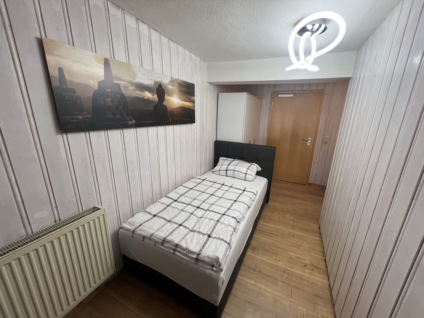 Un dormitorio con cama, un radiador, un cuadro y una puerta.