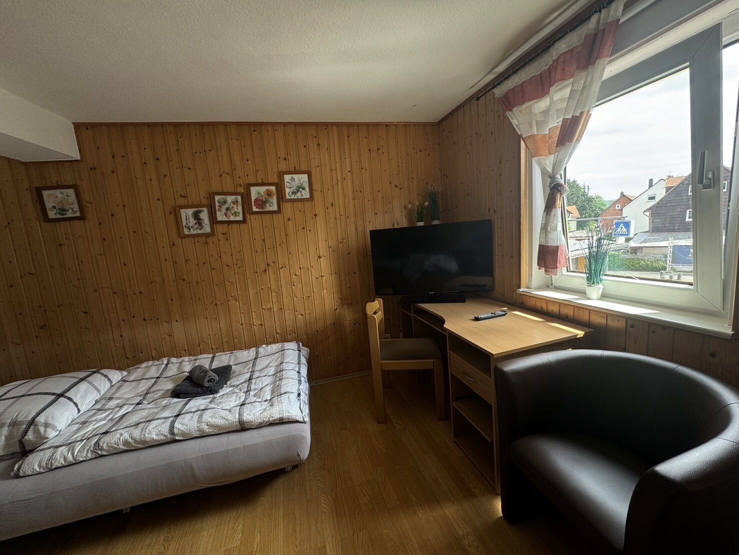 Ein kleines Zimmer mit einem Bett, einem Schreibtisch, einem Stuhl und einem Fernseher.
