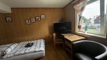 Ein kleines Zimmer mit einem Bett, einem Schreibtisch, einem Stuhl und einem Fernseher.