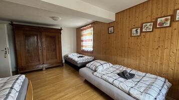 Une chambre avec deux lits, un plancher en bois, une armoire et une fenêtre avec des rideaux.