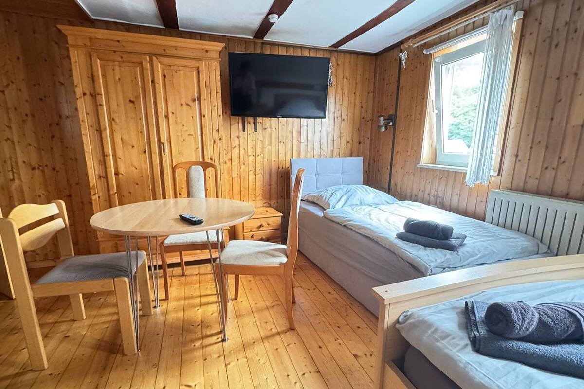 A cozy cabin with a wooden interior, a dining table with chairs, a bed with a pillow, and a TV mounted on the wall.