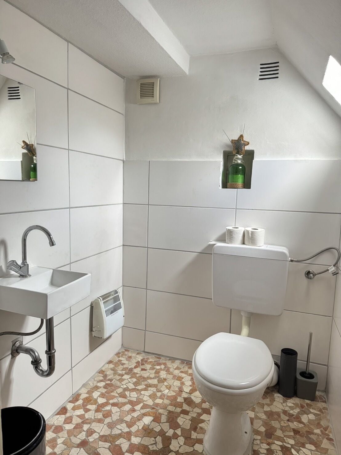 Une salle de bain avec un lavabo blanc, des toilettes et un sol carrelé orné d’un motif en mosaïque.