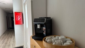 A coffee machine on a wooden cabinet with a tray of cups and a red fire extinguisher on the wall. - Gasthaus Nangfa Engel  (Edermünde)