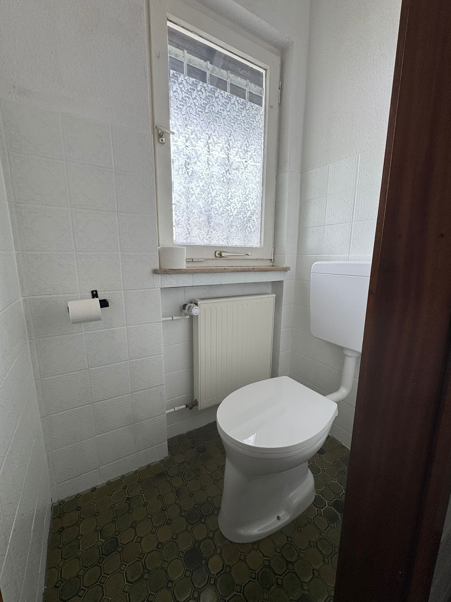 Un baño pequeño con inodoro, ventana y radiador.