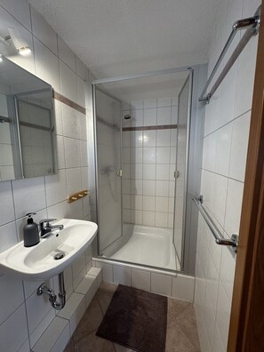 A bathroom with a glass-enclosed shower, a white sink with a soap dispenser, and a mirror. - Gasthaus Nangfa Engel  (Edermünde)