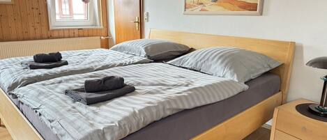 A double bed with grey bedding, a wooden headboard, and a nightstand with a lamp.