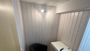 A small, compact room with a wooden floor, a black chair, a white desk, and a door. - Gasthaus Nangfa Engel  (Edermünde)