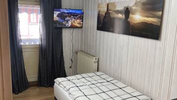 Ein Schlafzimmer mit einem Bett, einem an der Wand montierten Fernseher, einem Fenster mit Vorhängen und einer Heizung.