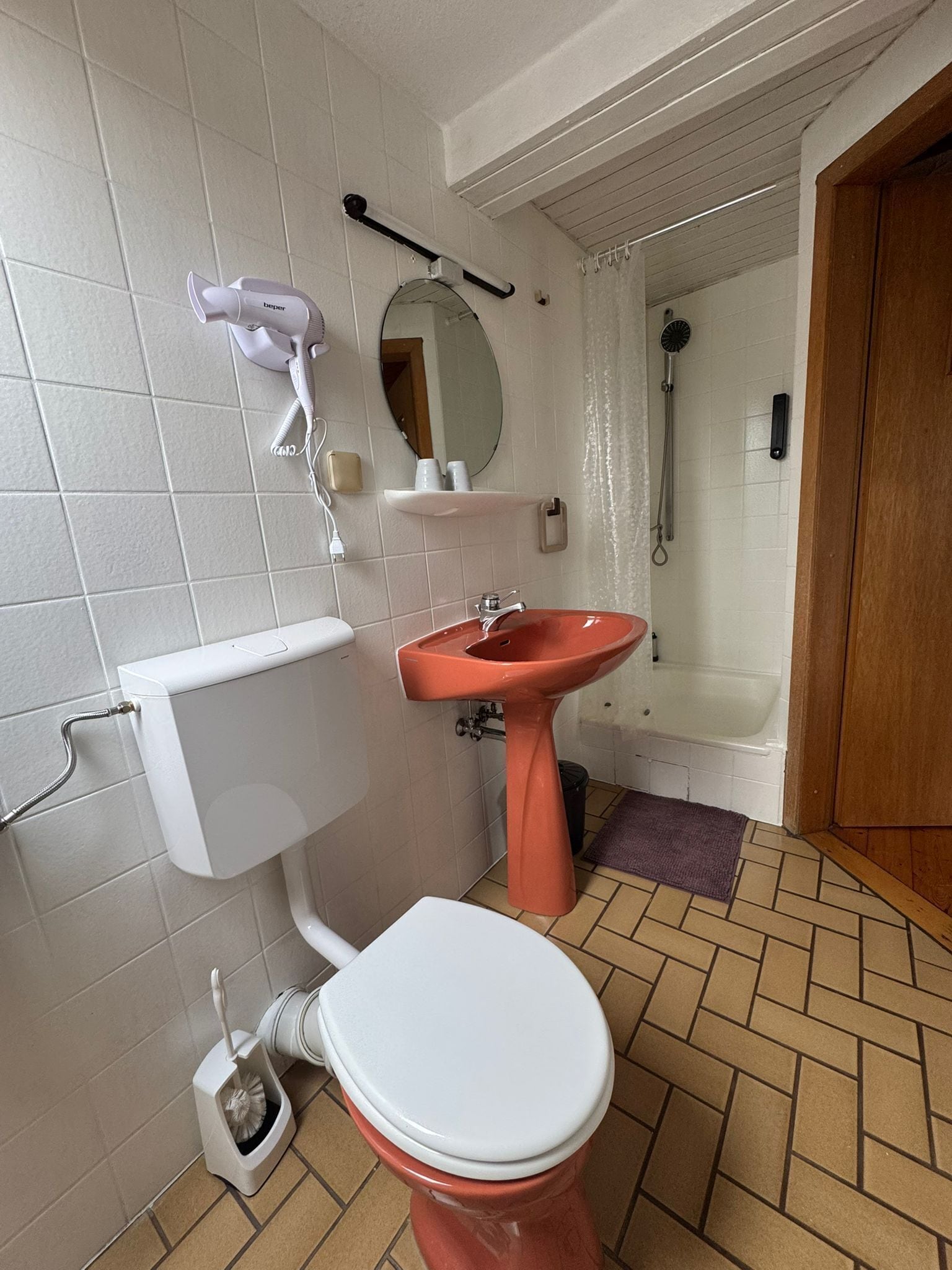 Un baño con inodoro blanco, lavamanos rojo y zona de ducha.