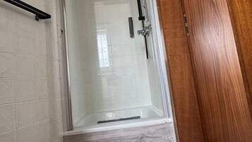 Ein Badezimmer mit Duschkabine aus Glas, einer Holztür und einem Marmorboden.