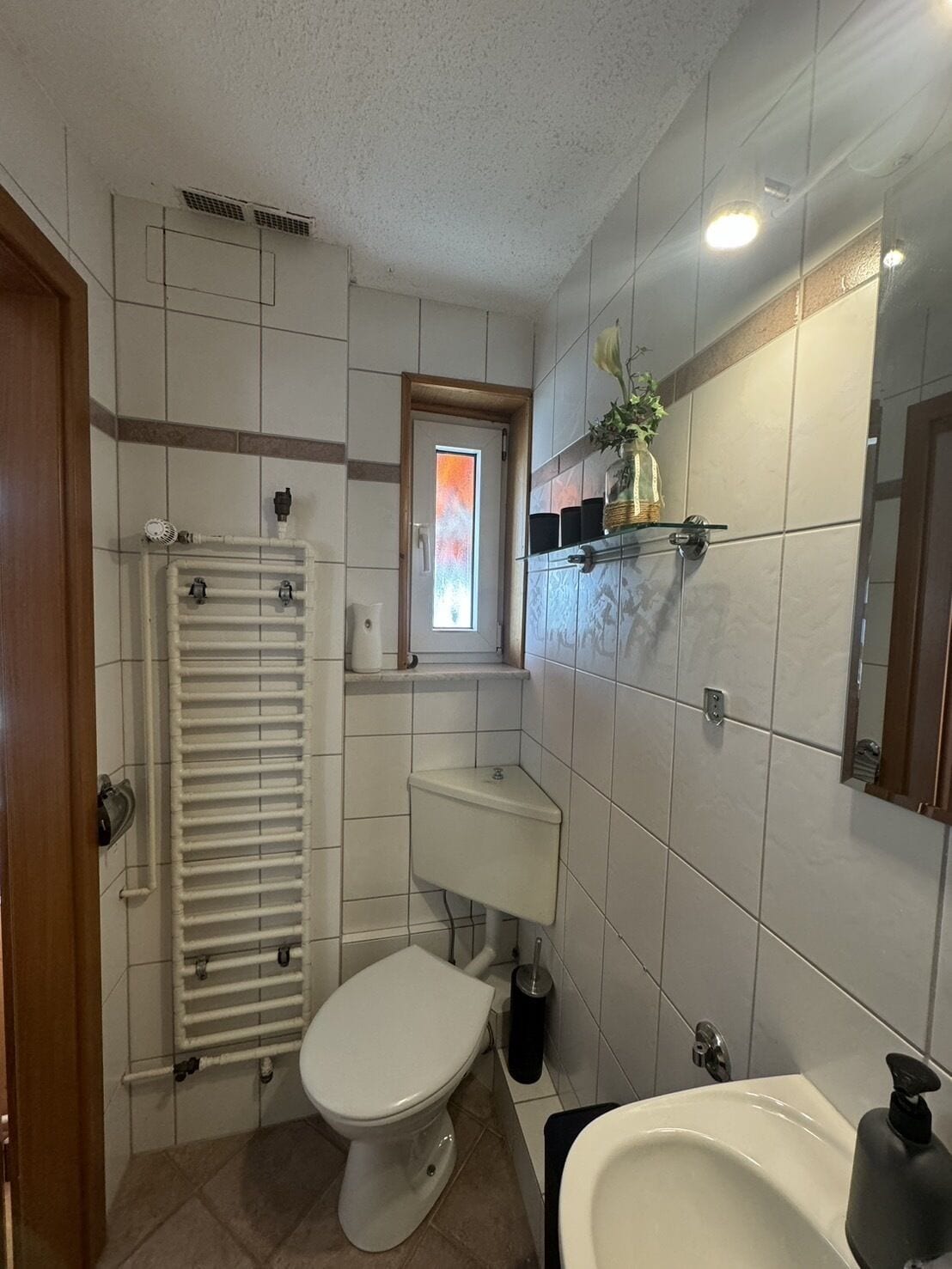 A bathroom with a toilet, sink, and shower. There is a window with a view of the outside.