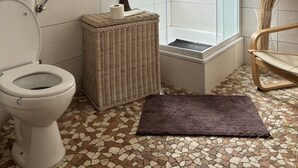 A bathroom with a glass-enclosed shower, a toilet, a wicker stool, and a chair. - Gasthaus Nangfa Engel  (Edermünde)
