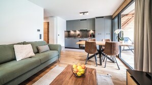 Un salon moderne avec un canapé vert, un coin repas avec une table et des chaises en bois, et une cuisine avec des meubles gris.