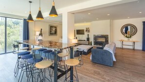 A modern living room with a large TV, a fireplace, and a dining area with bar stools.