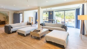 A spacious living room with a large sofa set, a coffee table, and a dining area with a view of the outdoors.