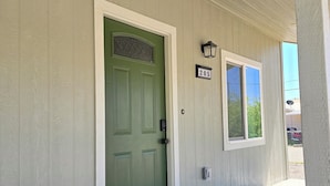 Uma porta verde com placa de identificação '205', um tapete de entrada com a palavra 'Welcome' e uma pequena janela com a placa '205'.