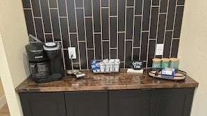 Uma cozinha compacta com cafeteira, xícaras de café e uma bandeja com cápsulas de café.