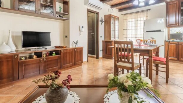 Un'ampia zona giorno con un mobile TV in legno, un tavolo da pranzo con sedie e un angolo cottura con mobili in legno.