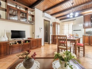 A spacious living area with a wooden TV stand, a dining table with chairs, and a kitchen area with wooden cabinets. - CASA VACANZE PERLA (Partinico)