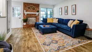 A modern living room with a blue sectional sofa, a patterned rug, and a brick accent wall. - The TX Oasis.  Boho Paradise.  Huge Backyard. (San Antonio)