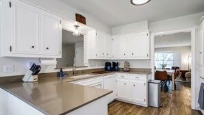A modern kitchen with white cabinetry, a central island, and a dining area visible in the background. - The TX Oasis.  Boho Paradise.  Huge Backyard. (San Antonio)